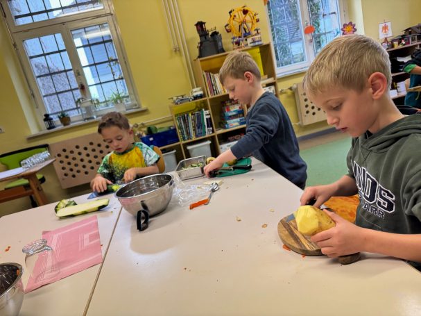 Erntedankessen Drei Kinder schneiden Gemüse und bereiten eine Mahlzeit in einer hellen Schulküche vor.