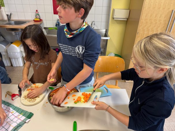 Erntedankessen Drei Kinder schneiden und bereiten gemeinsam Zutaten in einer Küche vor.
