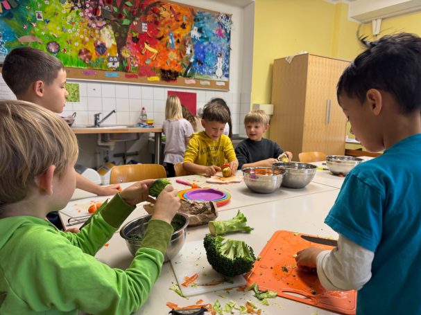 Erntedankessen Kinder bereiten gemeinsam in einer Küche frisches Gemüse vor. Bunte Wandmalerei im Hintergrund.