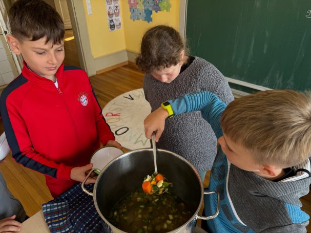 Erntedankessen Kinder kochen zusammen und rühren Gemüse in einem großen Topf.